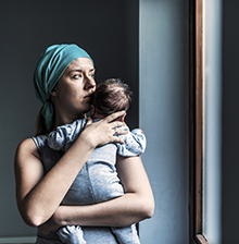 Caucasian Pensive Woman in headscarf, fighting breast cancer while holding her newborn baby relaxing in cancer treatment hospital, patient standing next to hospital window. Mother and baby son. Sleepy little child with serious mom.